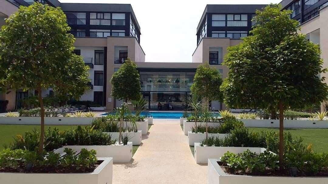 Un edificio moderno con un'ampia vetrata centrale, circondato da un paesaggio simmetrico e una piscina.