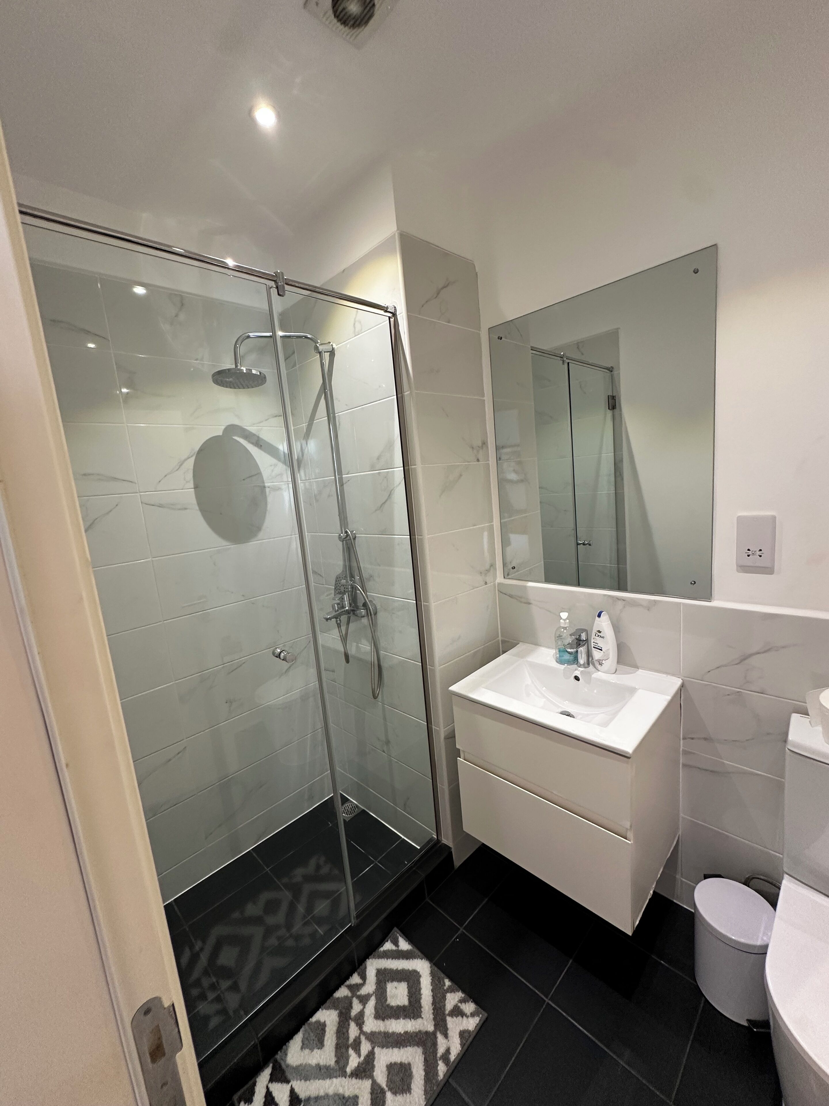 Une salle de bain moderne avec une douche à parois de verre, un lavabo blanc et des toilettes.