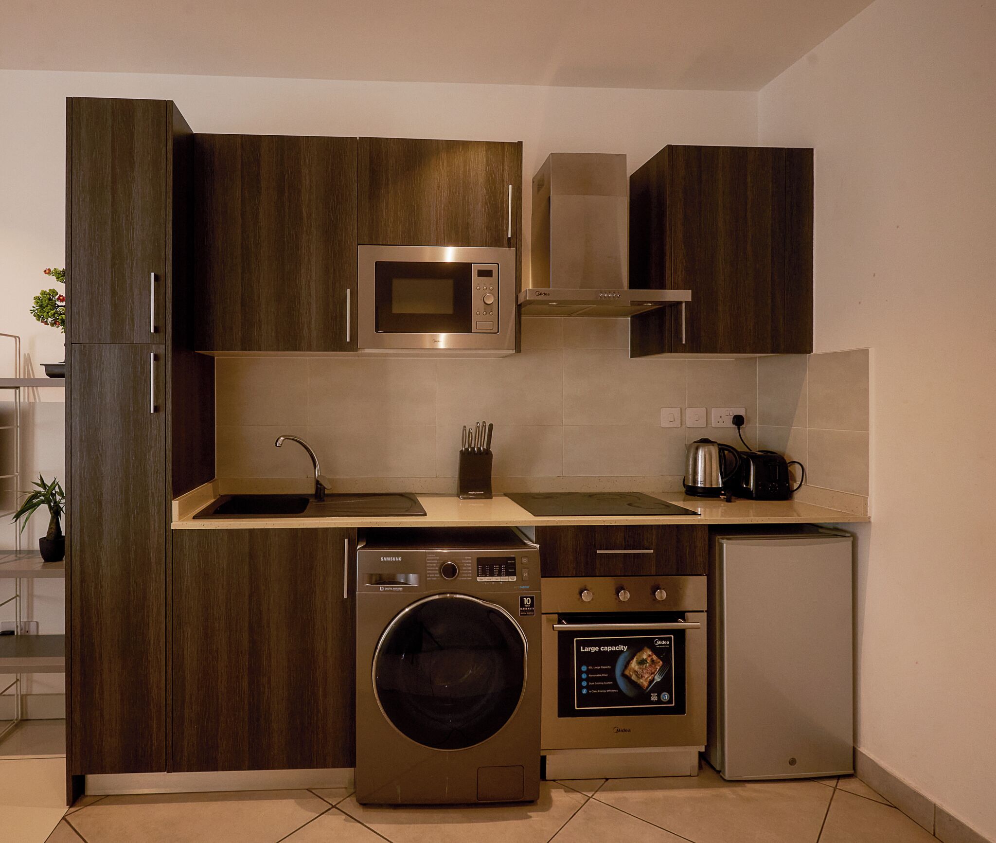 A compact kitchen with a microwave, oven, washing machine, and a small refrigerator.