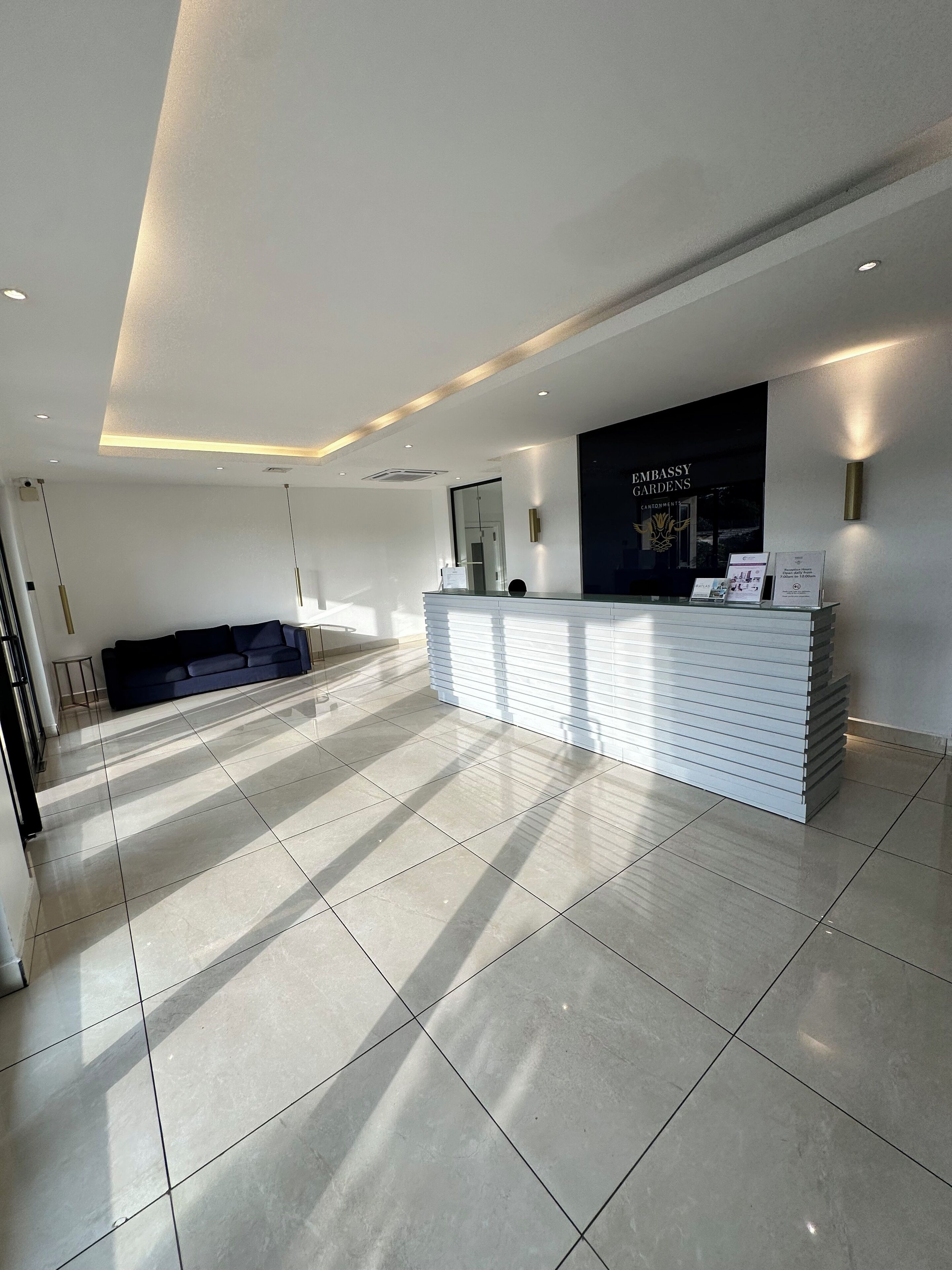 Zona d'estació elegant i moderna, amb un taulell de recepció blanc, un sofà blau fosc i un gran finestral amb llum natural.