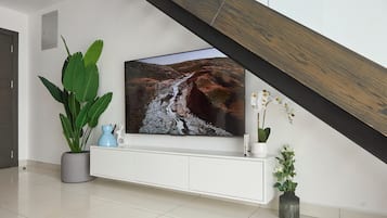 A modern living room with a large flat-screen TV mounted on a white console, a potted plant, and a vase with flowers.