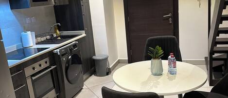A modern kitchen with stainless steel appliances, a dining area with a round table and black chairs, and a dark wooden door.