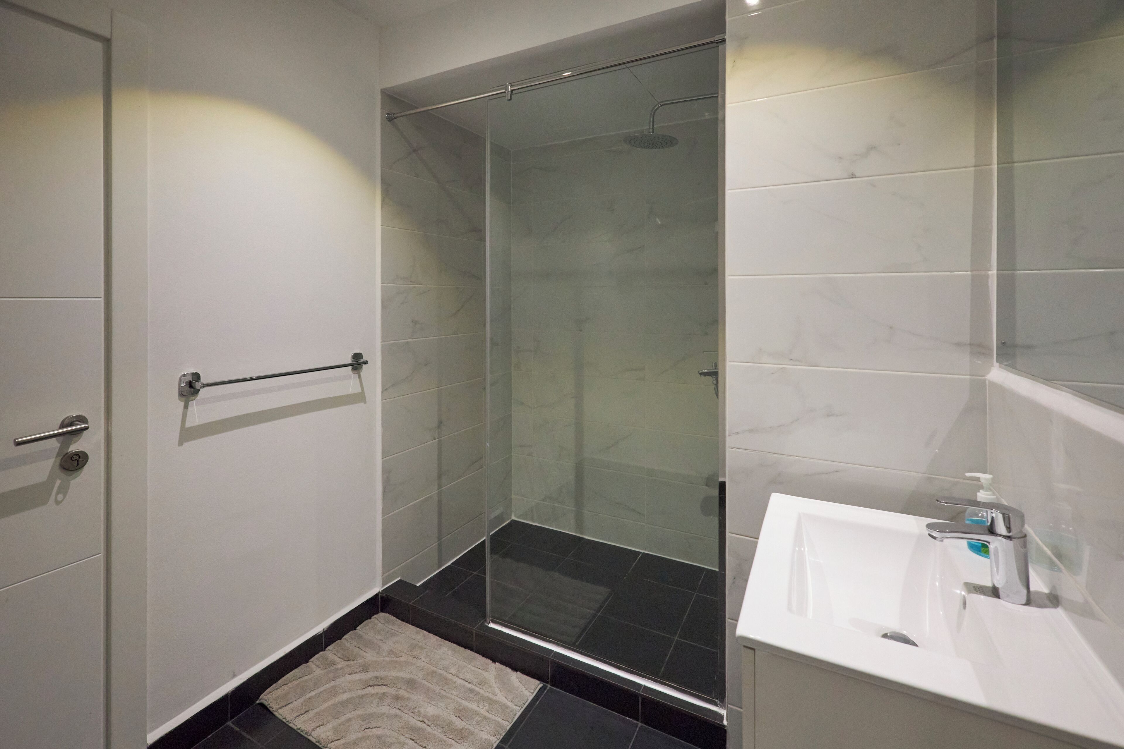A modern bathroom with a glass-enclosed shower, a white sink, and a towel rack.