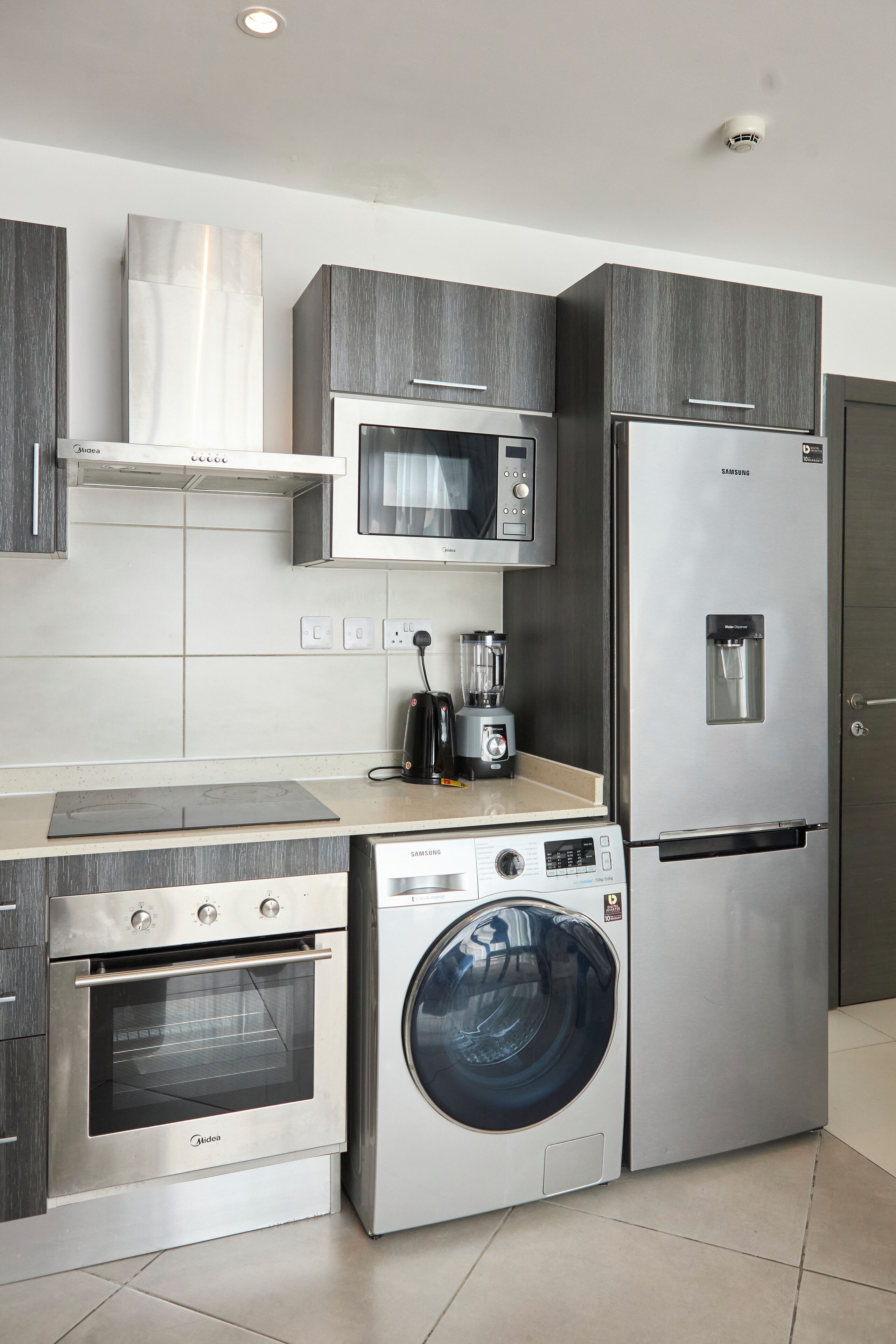 A modern kitchen with a built-in microwave, stainless steel refrigerator, oven, and washing machine.