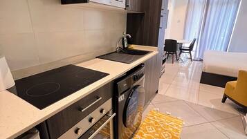 A modern kitchen with a built-in microwave, oven, and dishwasher. There is a dining area with a table and chairs, and a yellow armchair.