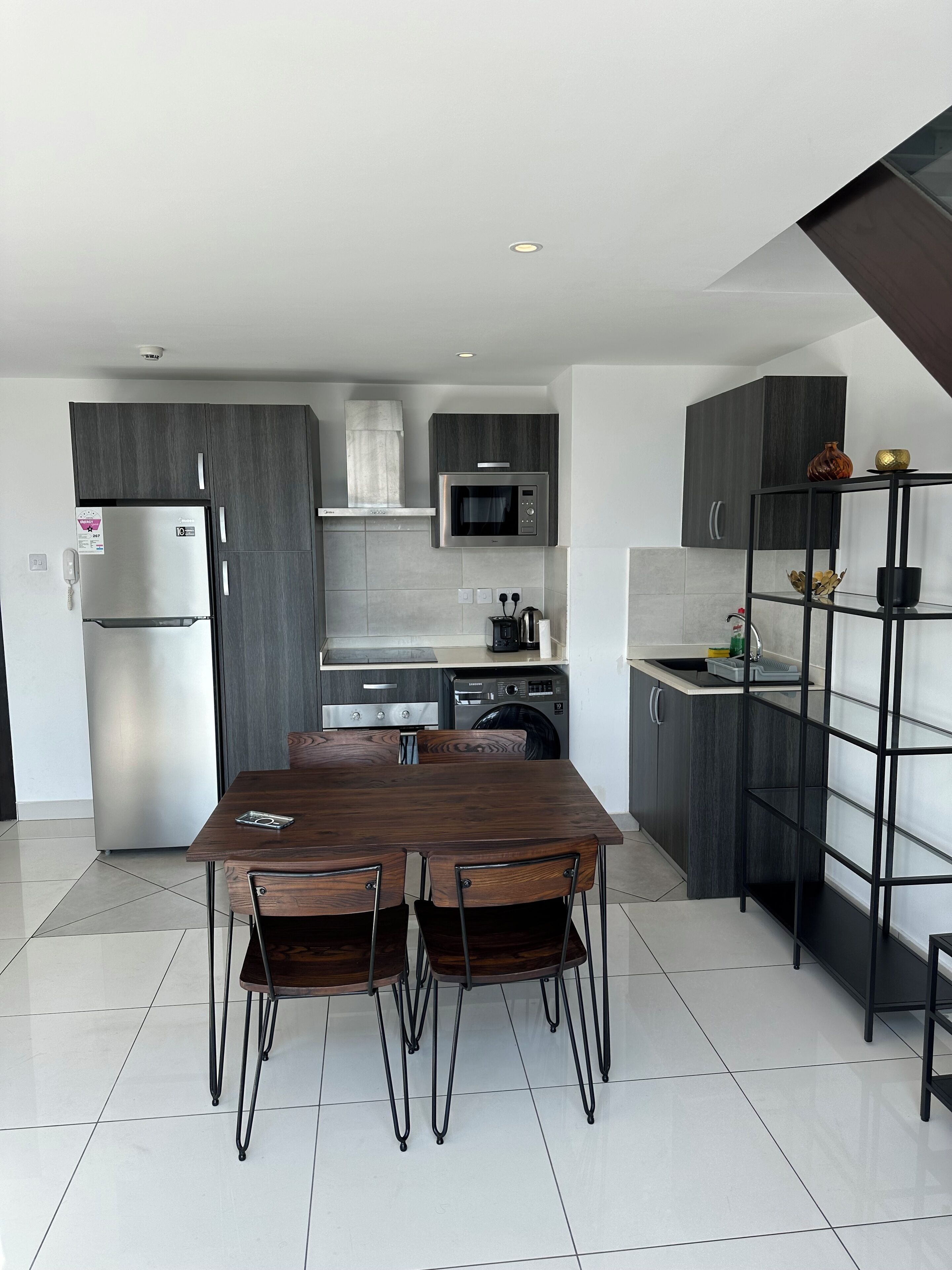 A modern kitchen with dark wood cabinets, stainless steel appliances, and a dining area with a wooden table and chairs.