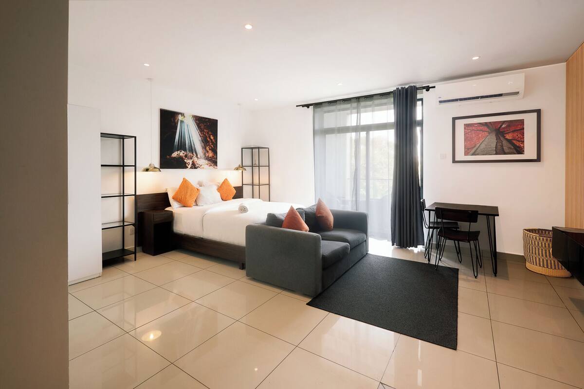 A modern hotel room with a bed, sofa, desk, and chairs.