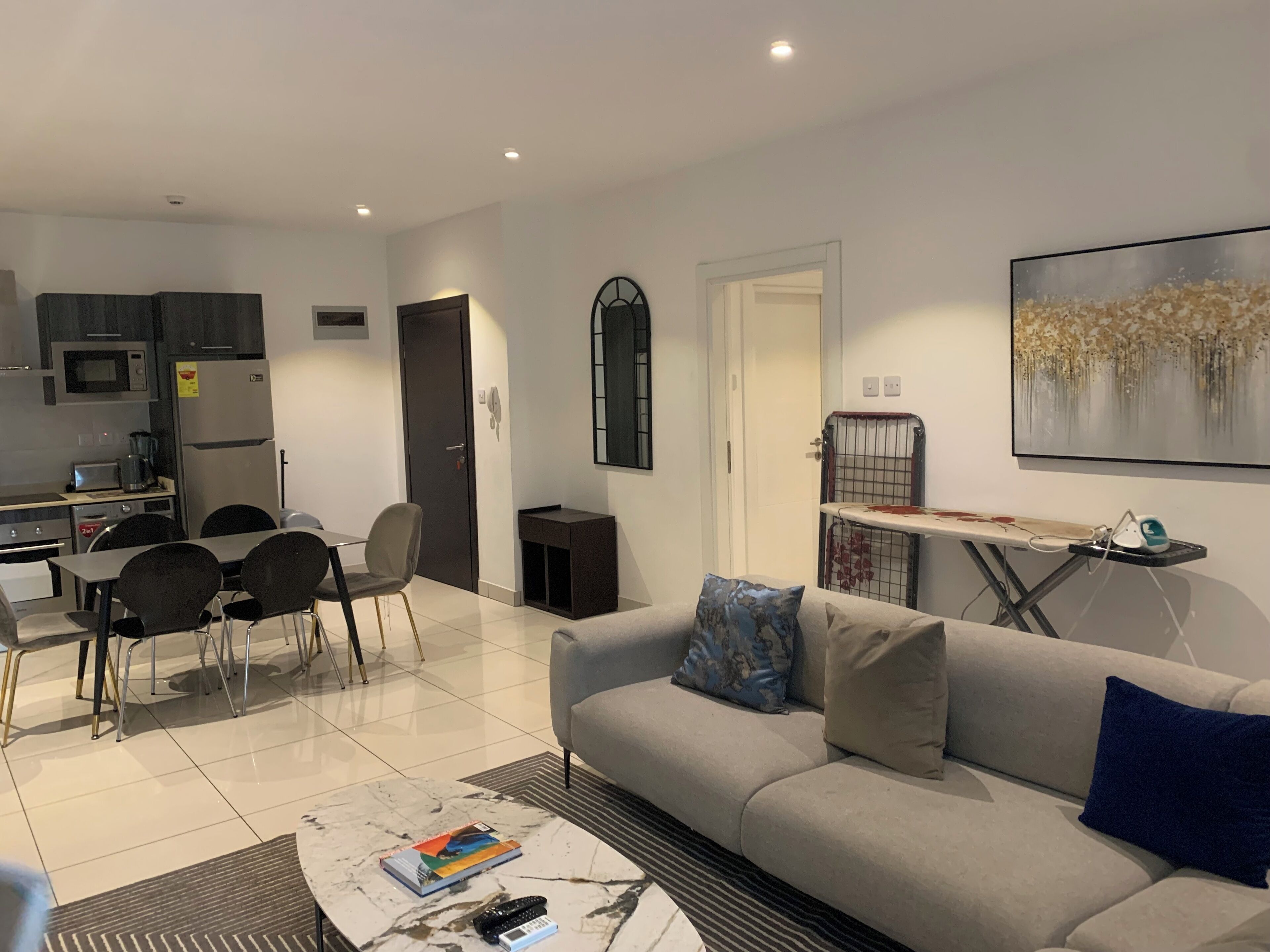 A modern living room with a grey sofa, a coffee table, and a dining area with chairs and a small kitchen in the background.