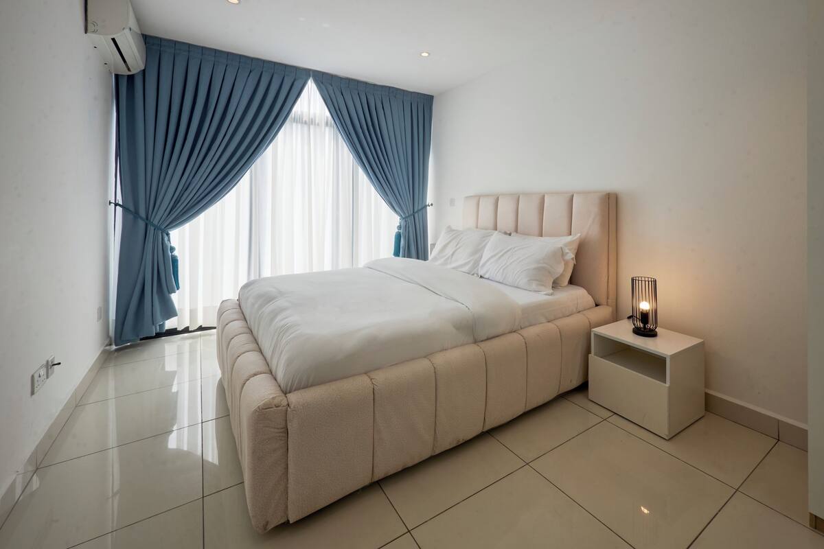 A modern bedroom with a large bed, a nightstand, and a wall-mounted air conditioner.
