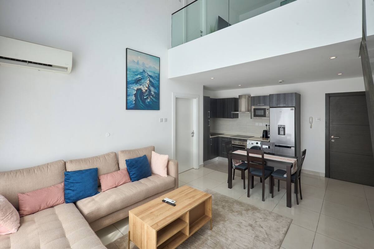 A modern living room with a sofa, coffee table, and a dining area with chairs and a table.