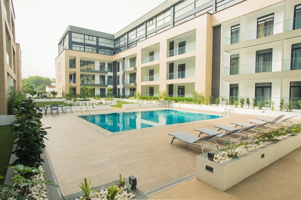 A modern building with a swimming pool, lounge chairs, and outdoor seating.