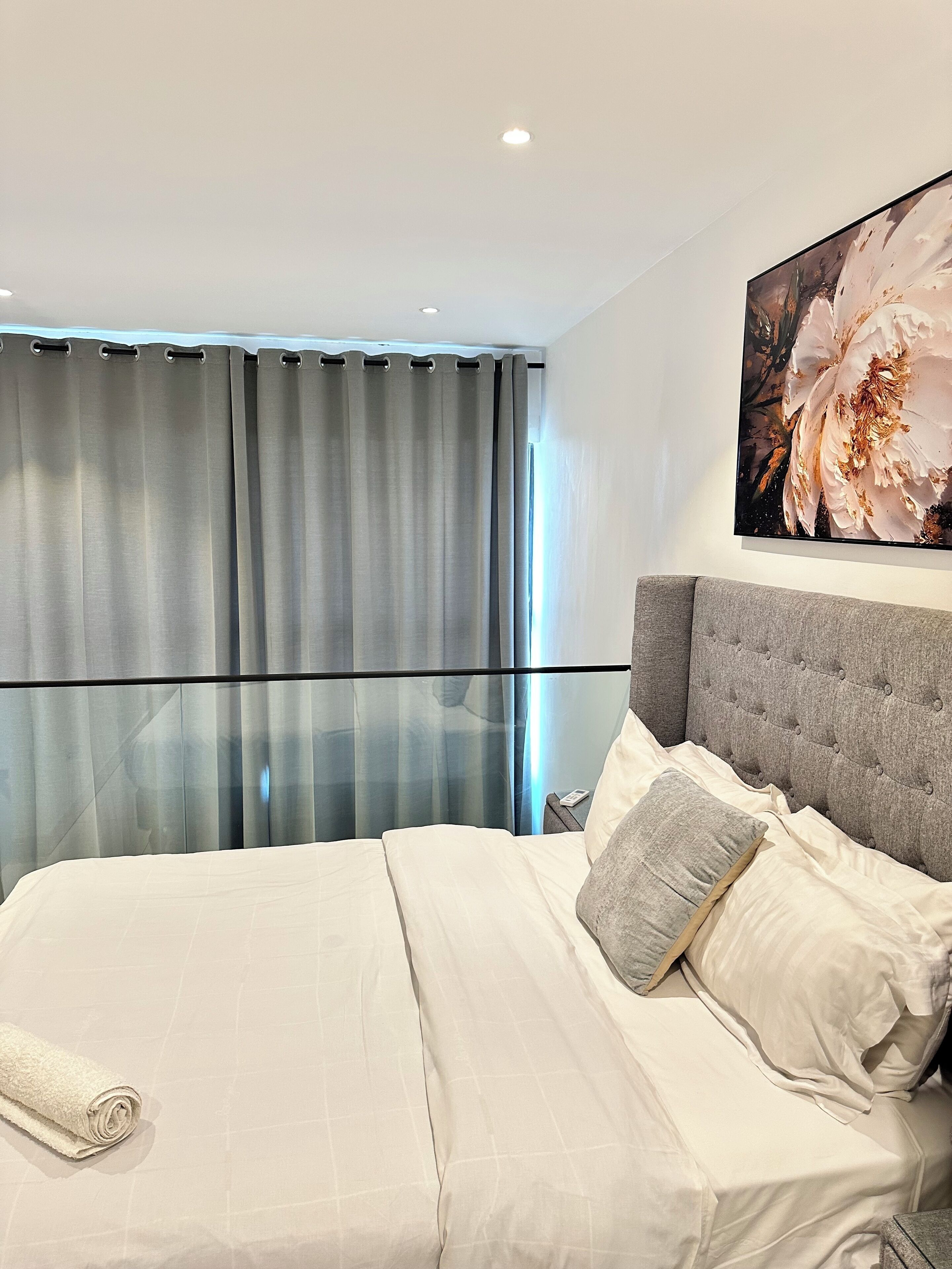 Une chambre d’hôtel moderne avec un grand lit, des rideaux gris et une œuvre d’art florale accrochée au mur.