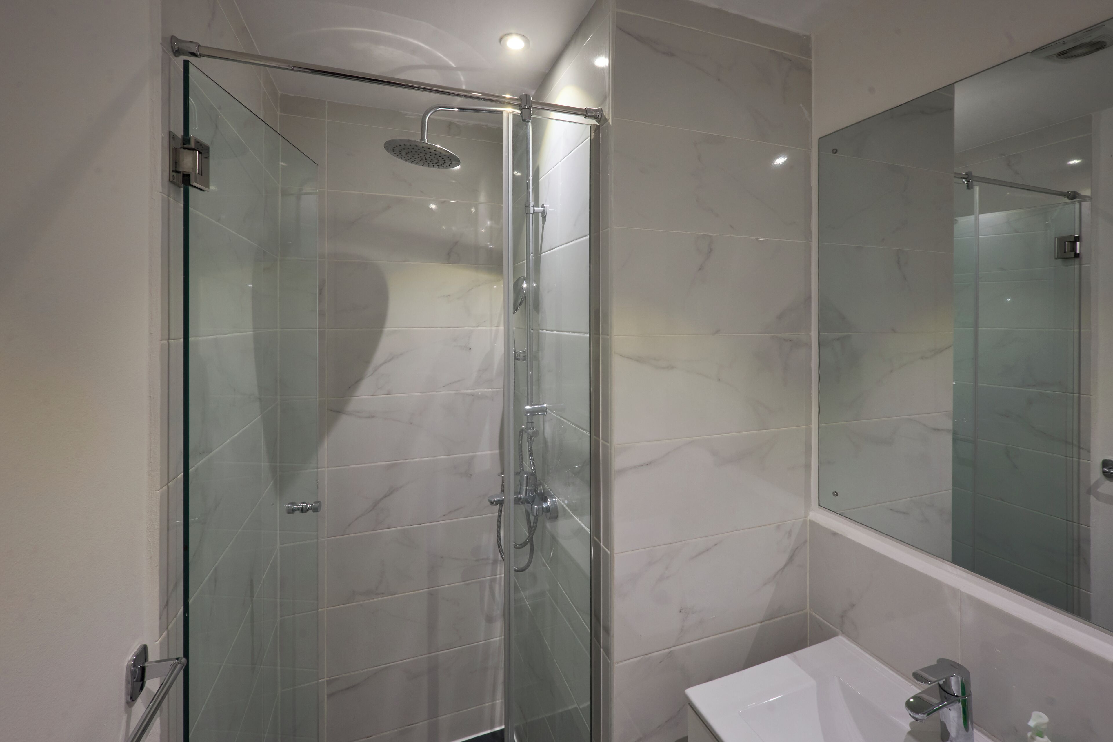 A modern bathroom with a glass-enclosed shower, a white sink, and a large mirror.