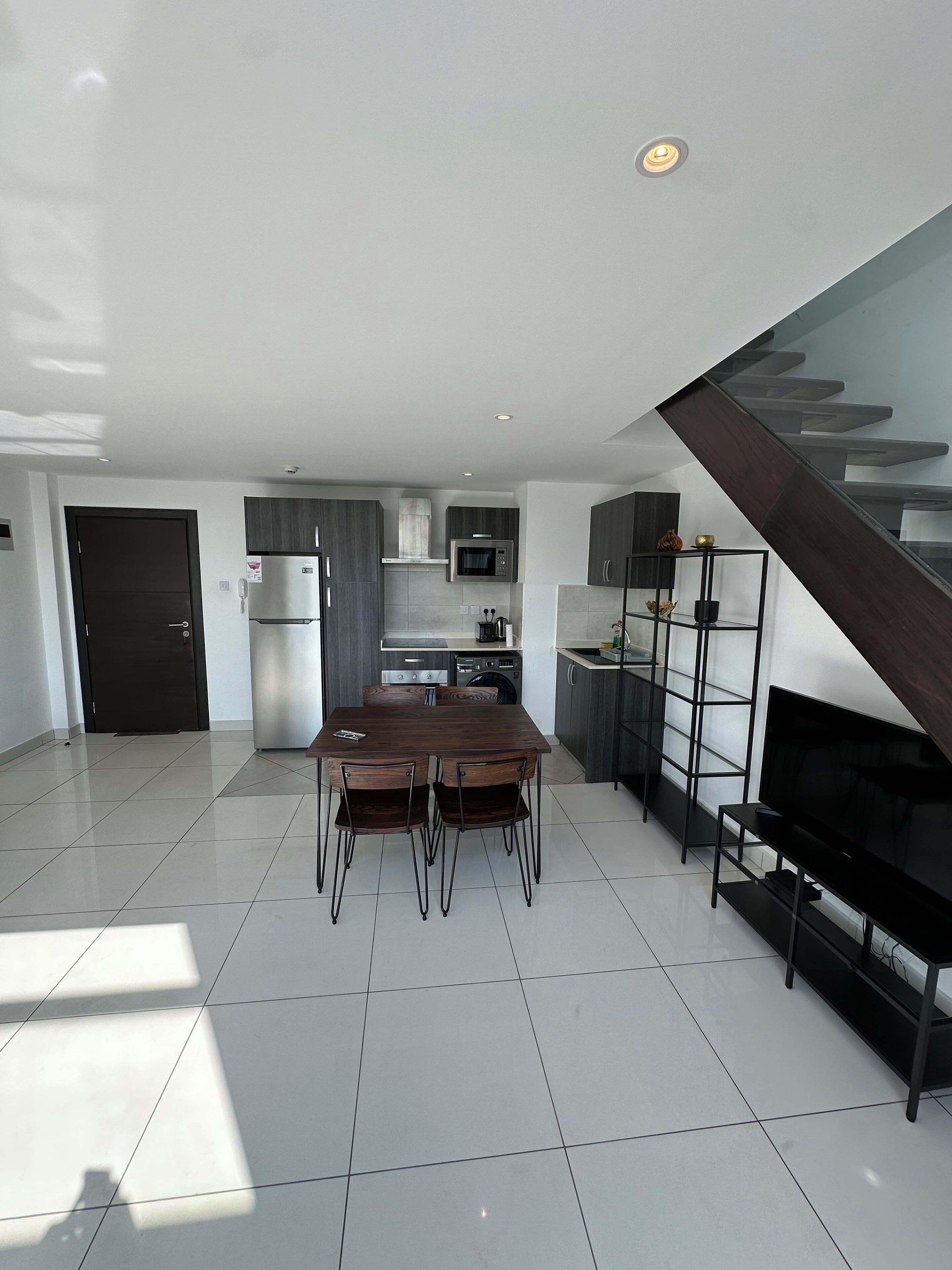 A modern kitchen with a dining area, a staircase, and a TV.