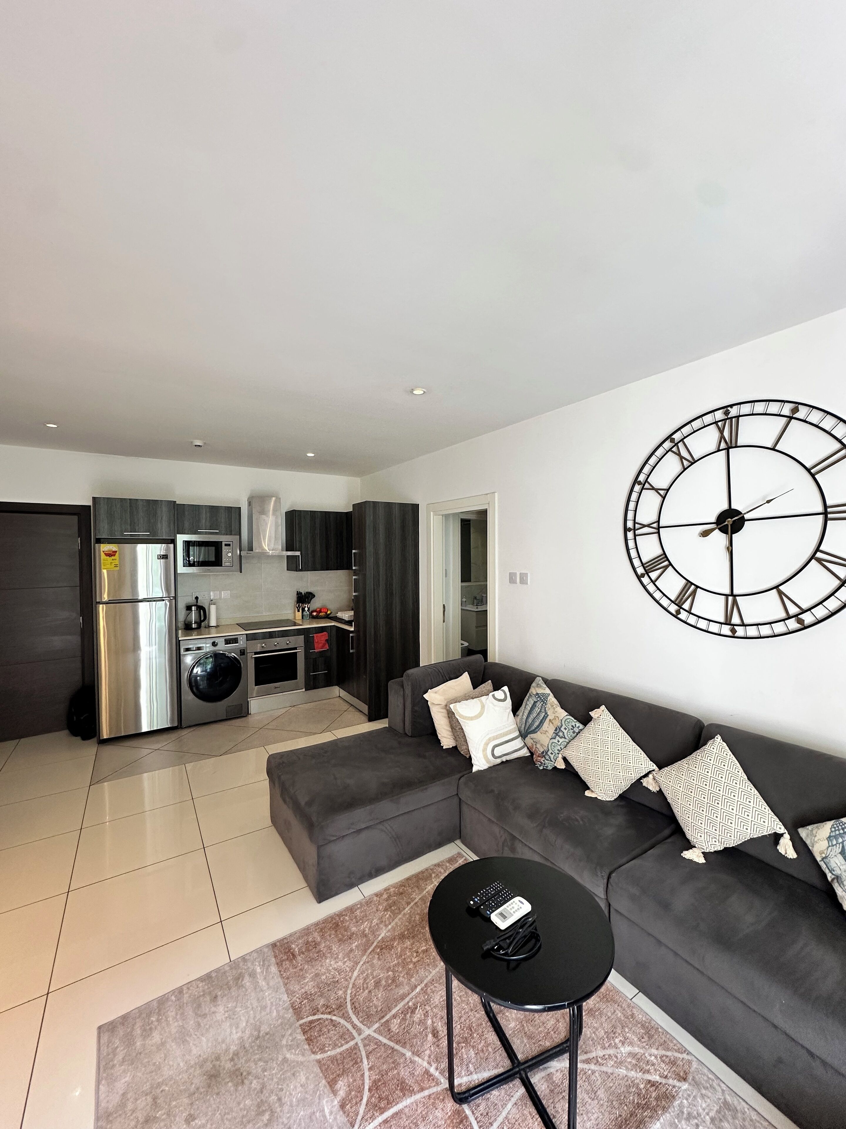A modern living room with a grey sofa, a black coffee table, and a large wall clock.