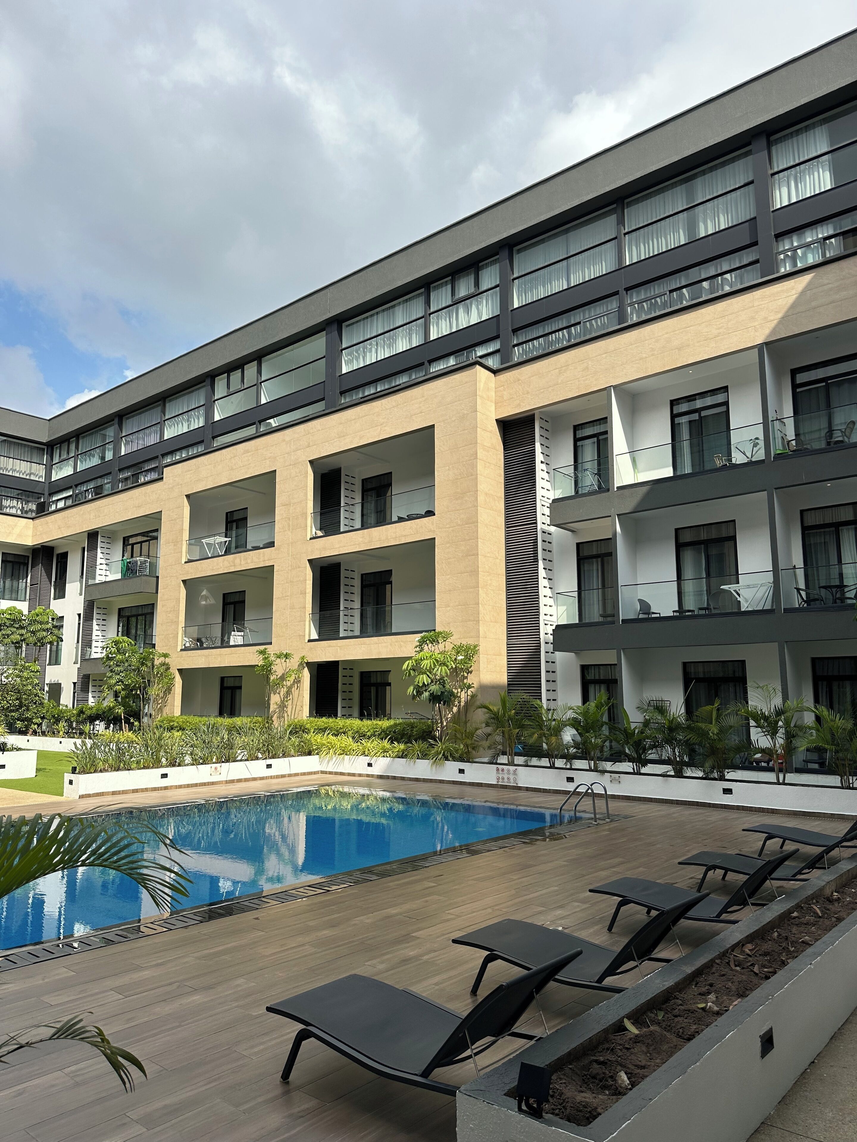A modern multi-story hotel with a swimming pool, outdoor seating, and balconies.