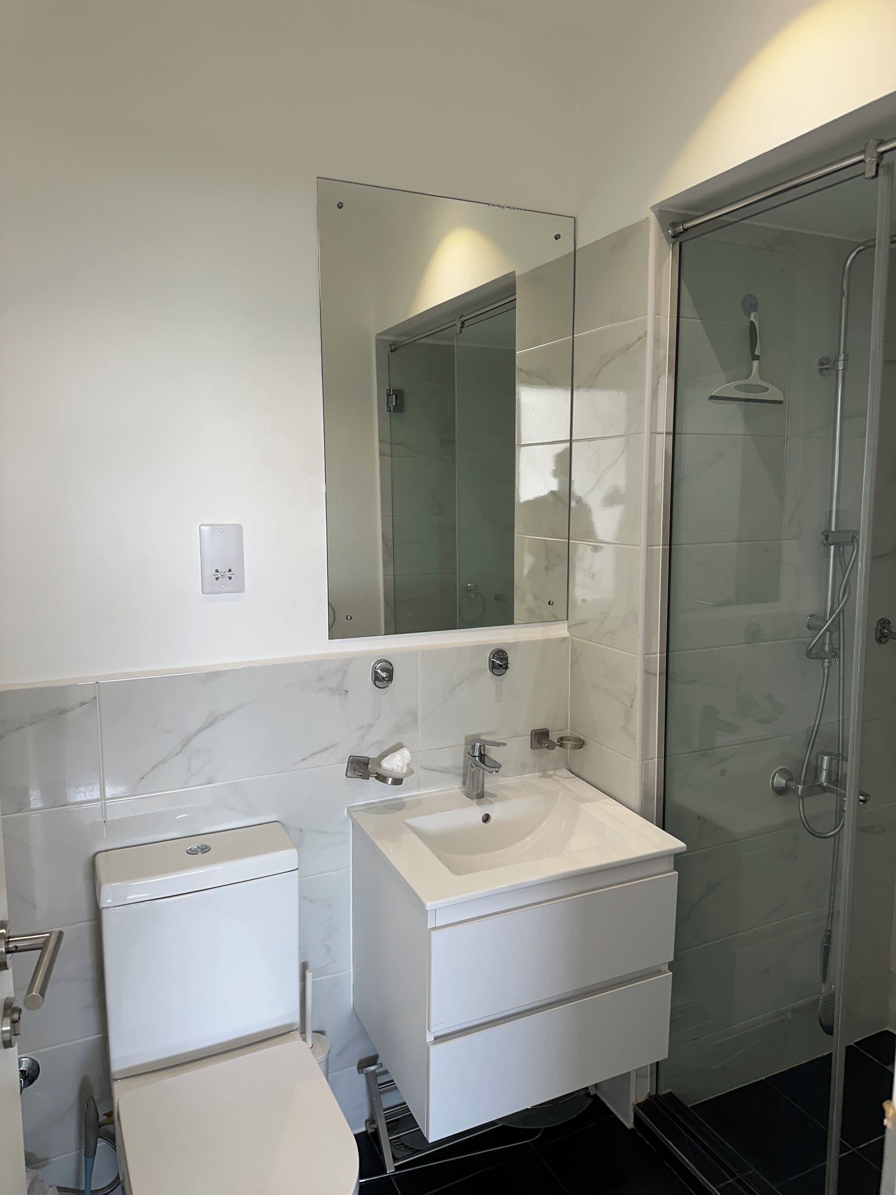A modern bathroom with a white sink, mirror, and glass shower enclosure.