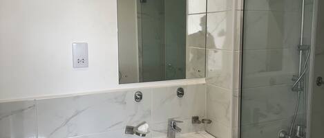 A modern bathroom with a white sink, mirror, and glass shower enclosure.