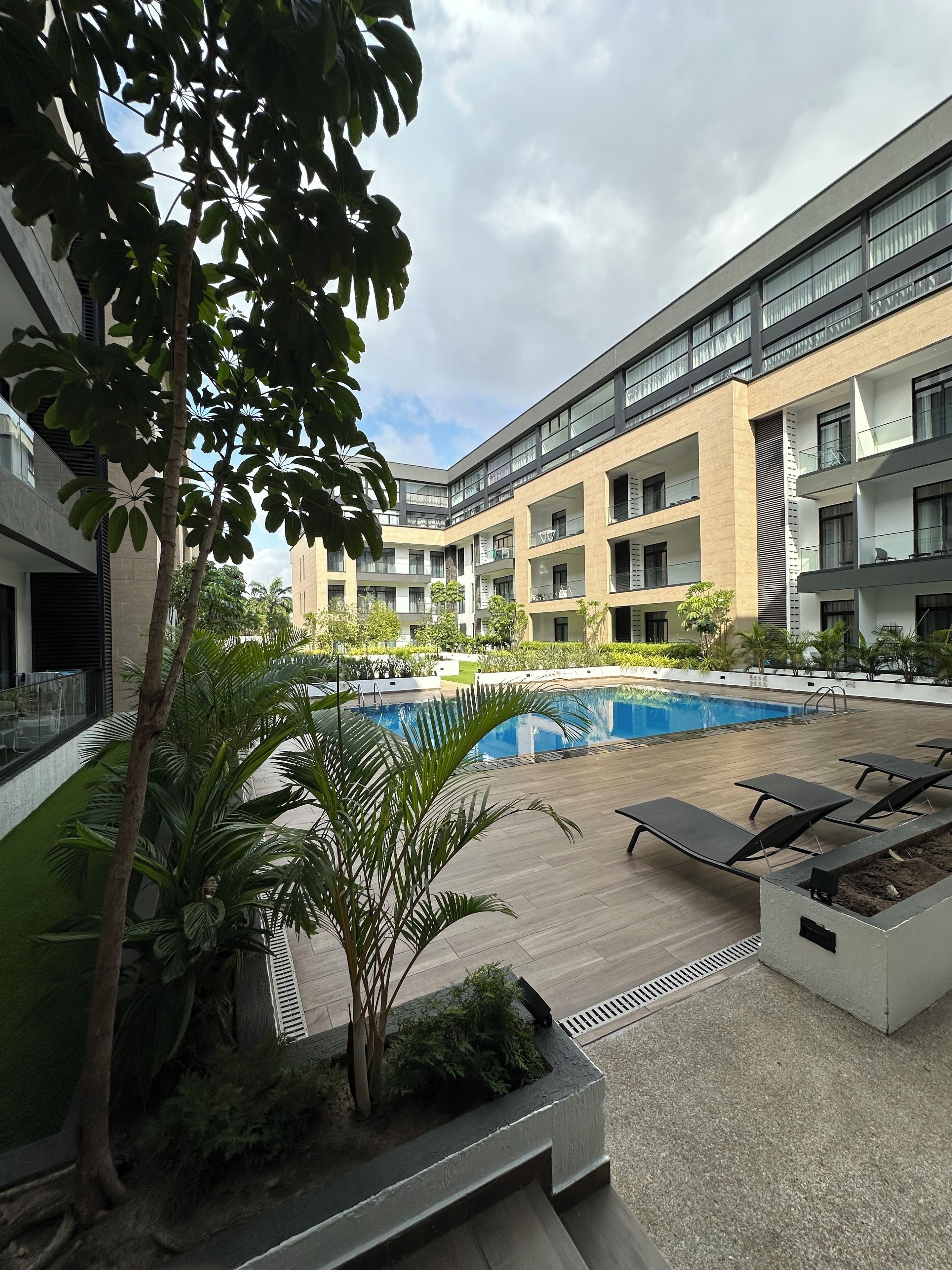 A modern building with a swimming pool, outdoor seating, and lush greenery.
