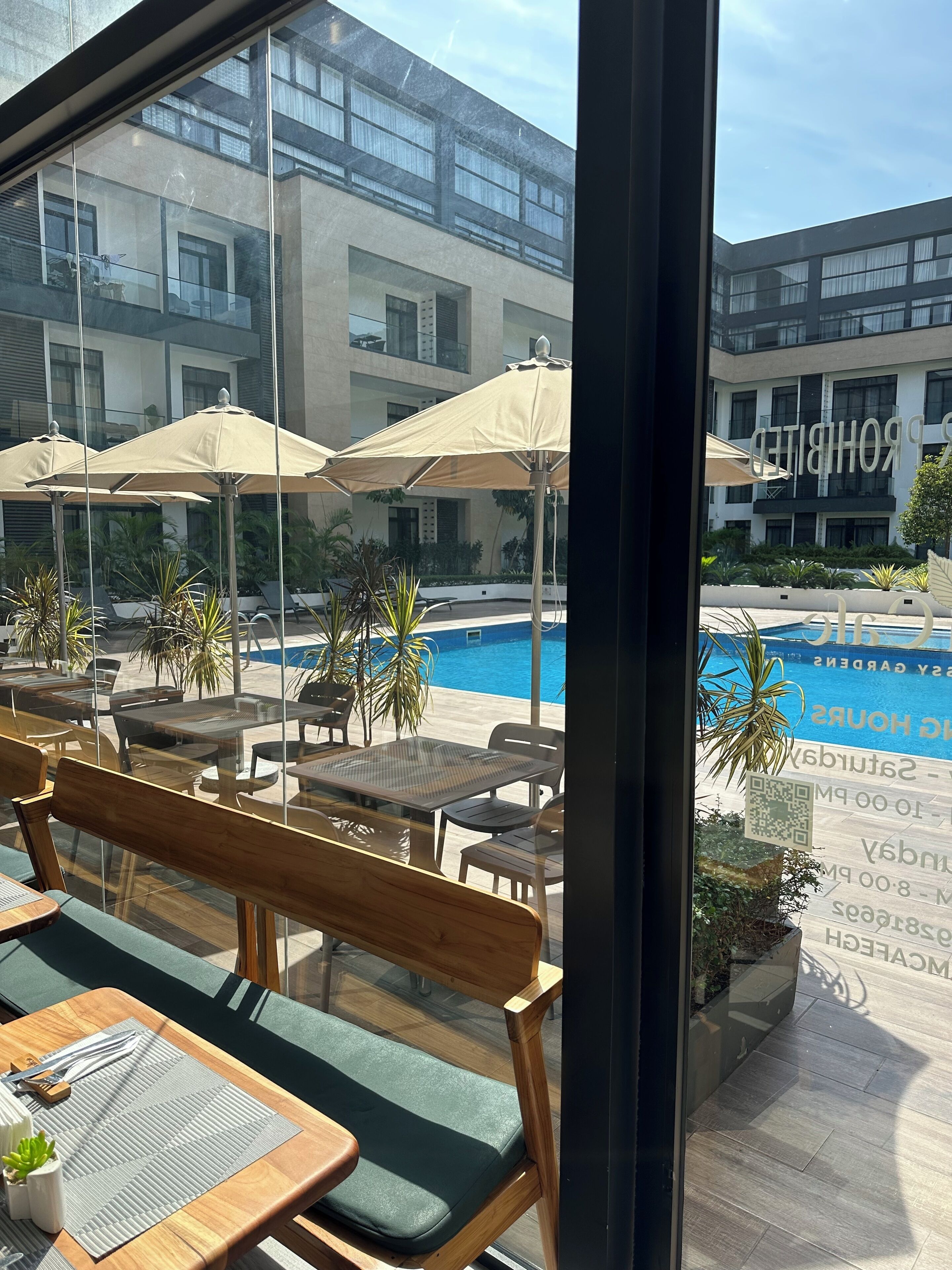 Un espace aménagé au bord de la piscine, avec des chaises longues et des parasols, une piscine, et un bâtiment sur lequel on peut voir, au fond, une enseigne portant l'inscription « PONDERING ».