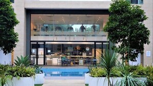 Un edificio moderno con fachada de vidrio, piscina y mobiliario exterior.