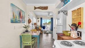 Une cuisine équipée d’une cuisinière, une table à manger avec des chaises, un luminaire suspendu et un tableau représentant des voiliers.
