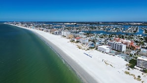 An aerial view of a coastal city with a long sandy beach, dense residential buildings, and a marina with boats. - ☀Beachfront Cottage, Upstairs 2BR🍹Walk to John's Pass🌊Large Covered Deck with Gu (Madeira Beach)