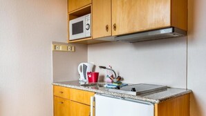A compact kitchen with wooden cabinets, a microwave, a kettle, and a small refrigerator. - Hotel Sterne - Apartment with Balcony (Beatenberg)