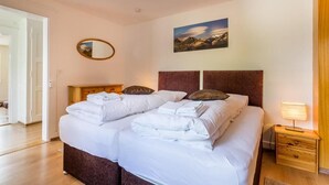 A neatly made double bed with white linens, a wooden headboard, and a small bedside table with a lamp. - Hotel Sterne - Apartment with Balcony (Beatenberg)