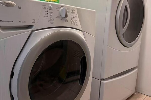 A front-loading Whirlpool washer with a control panel, a small green bottle, and a white wall in the background.