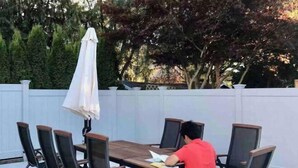 An outdoor dining area with a table and chairs, a white fence, and trees in the background. - Vancouver Garden Hotel (Richmond)