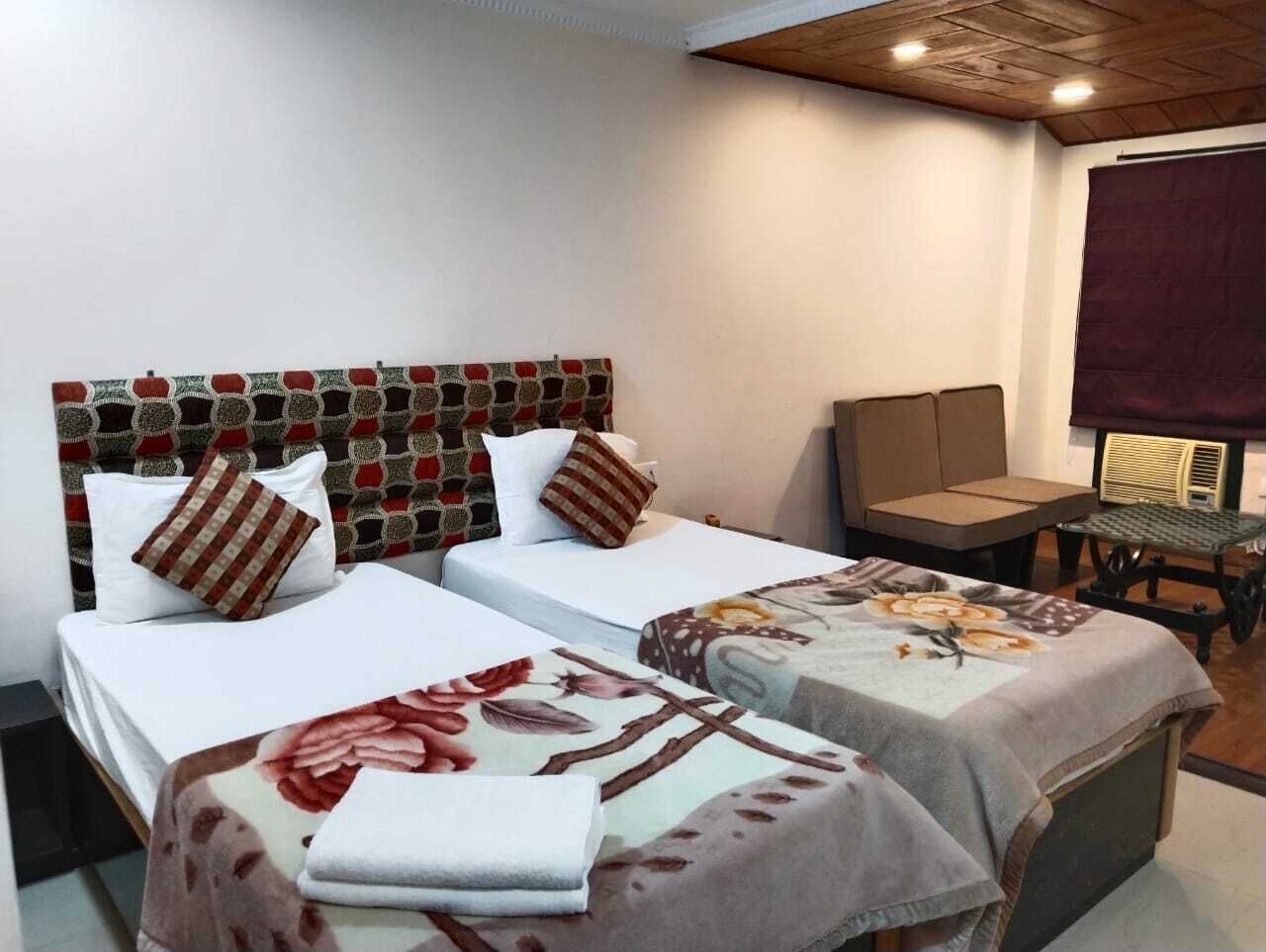 A hotel room with two single beds, a small table, a chair, and a large window.