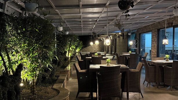 Un restaurante con mesas y sillas, un techo con diseño de cuadrícula y plantas colgantes.