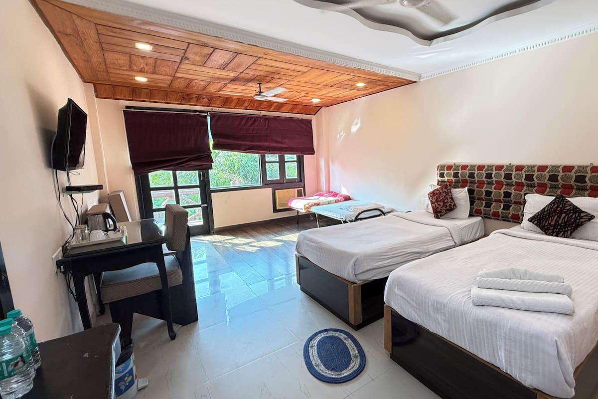 Habitación de hotel con dos camas, un escritorio, una silla, un televisor y una ventana con cortinas.
