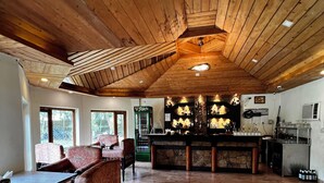 Una habitación amplia con un alto techo de madera, una zona de bar con encimera de piedra y un espacio de descanso con sillas estampadas.