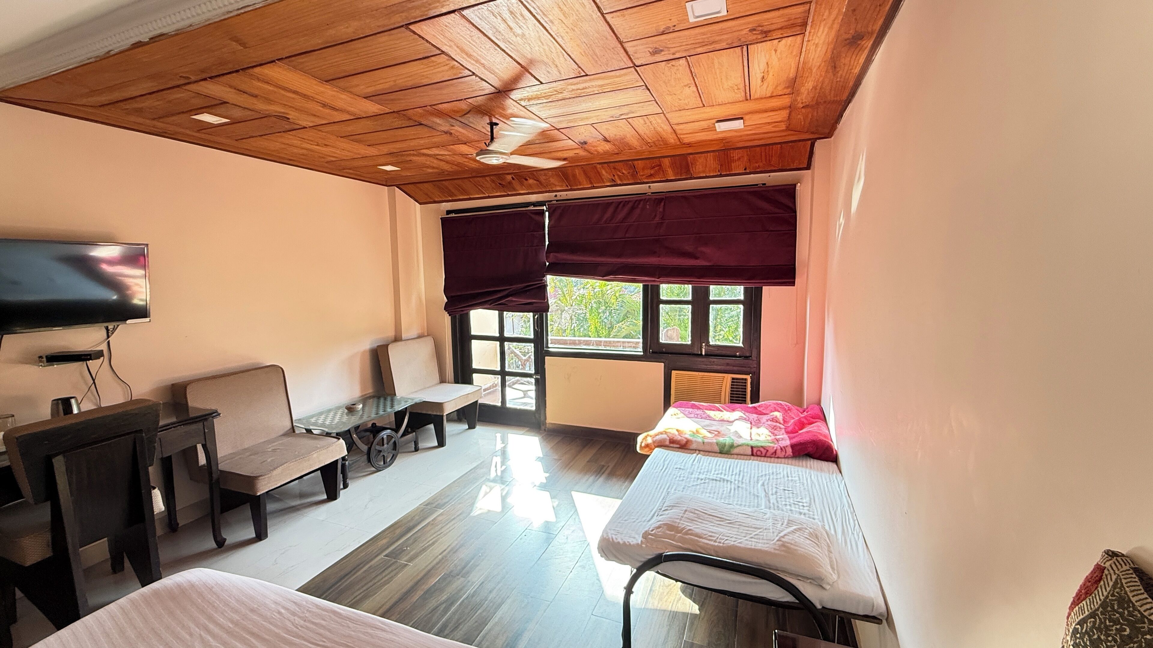 Ein Zimmer mit Holzboden, einem Fernseher, einem Bett, einem Tisch und Stühlen.