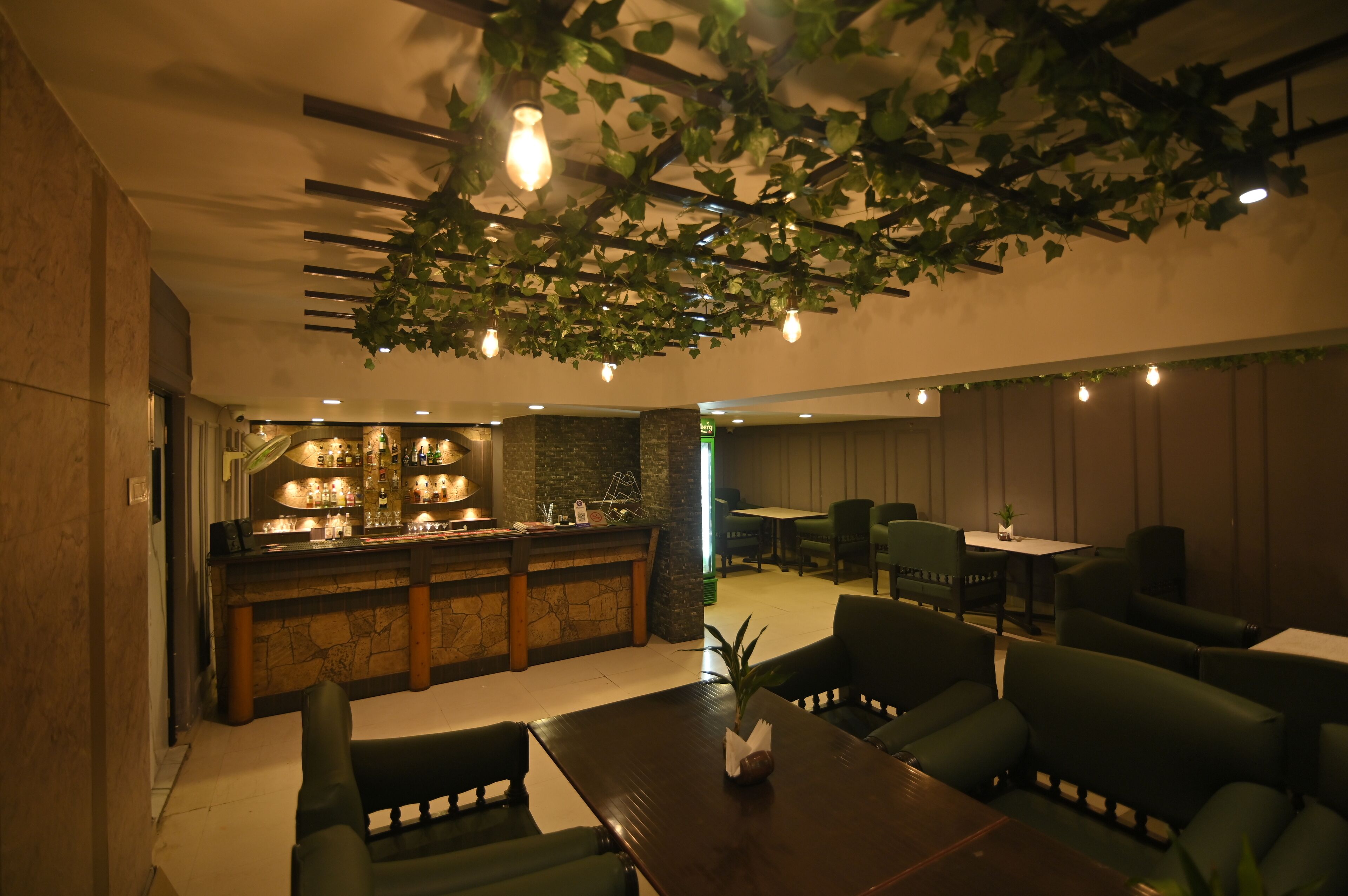 Zona bar con bancone in pietra, sedie rivestite in verde e lampade a sospensione.