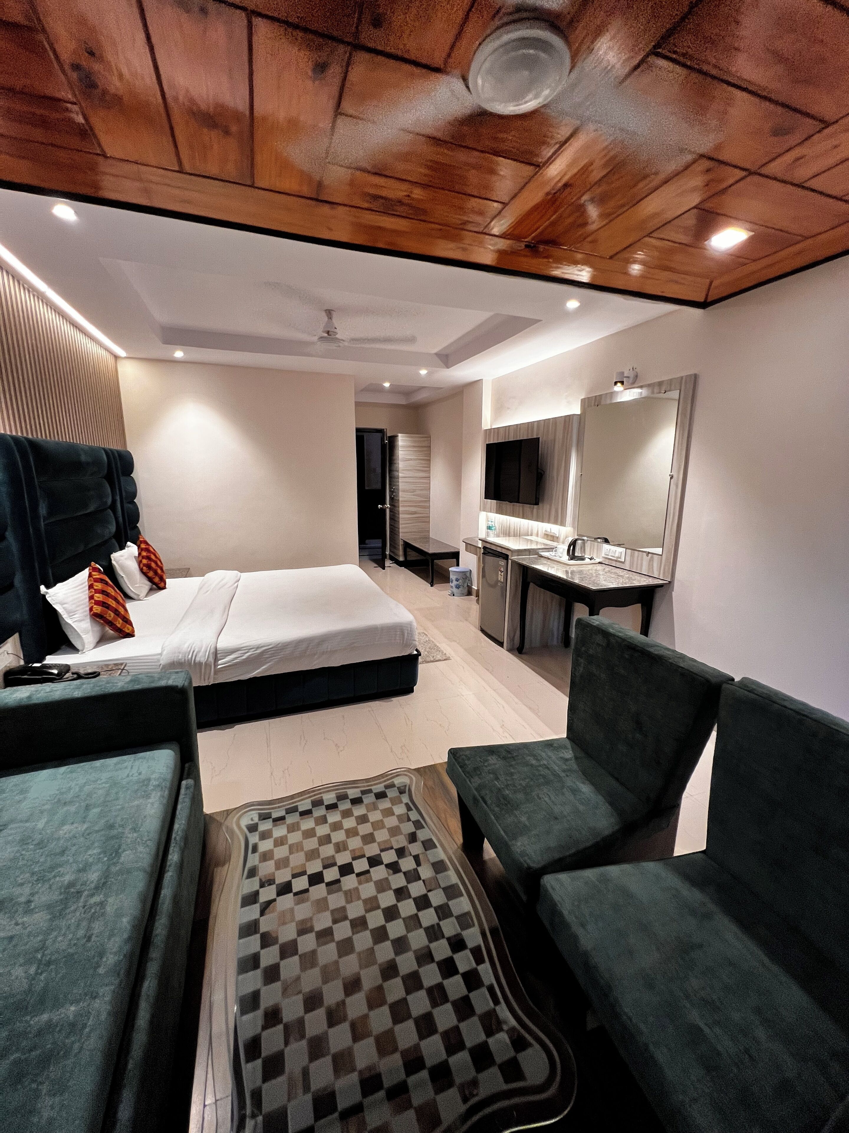Ein modernes Hotelzimmer mit einem Bett, zwei Sesseln, einem karierten Teppich, einem kleinen Tisch, einem Spiegel und einer Küchenzeile.