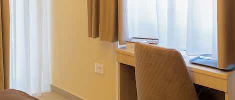 A hotel room with a bed, a desk with a chair, an air conditioner, and a window with curtains.