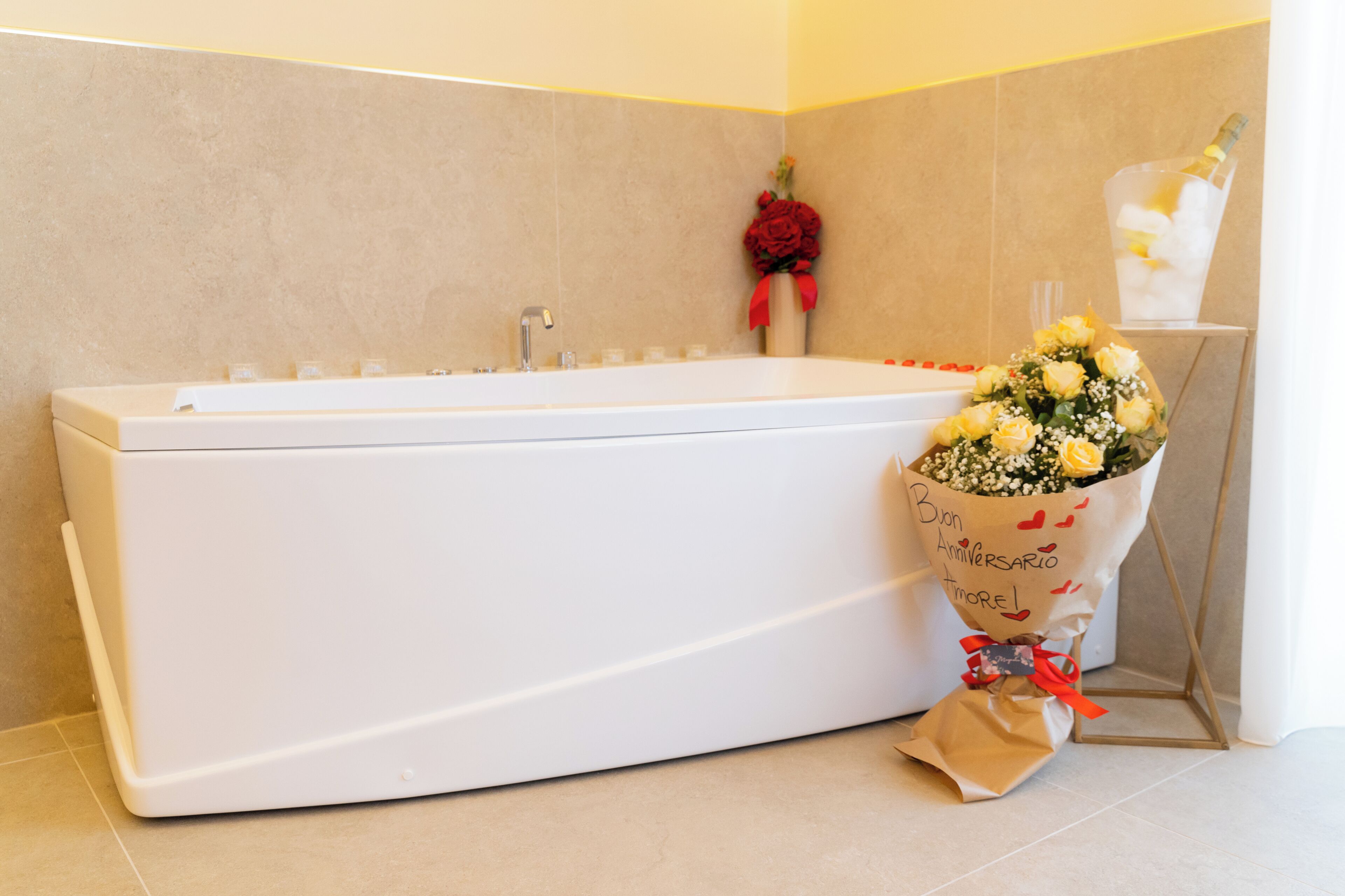 A bathroom with a white bathtub, a bouquet of flowers, and a bottle of champagne.