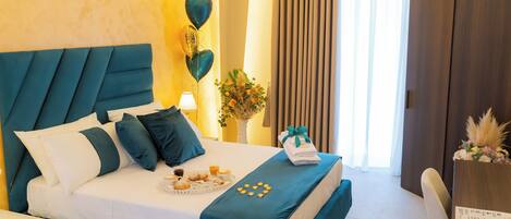 A neatly made bed with a teal headboard, a tray of pastries, and a small table with a vase of flowers.