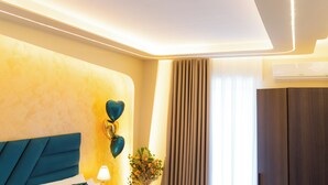 A modern hotel room with a blue headboard, a wall-mounted air conditioner, and a window with curtains. - Partenope's house (Ercolano)