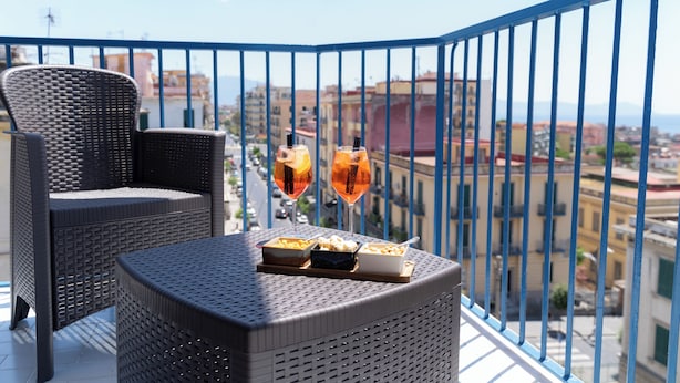 A balcony with wicker furniture, two glasses of a beverage, and a dessert tray. - Partenope's house (Ercolano)