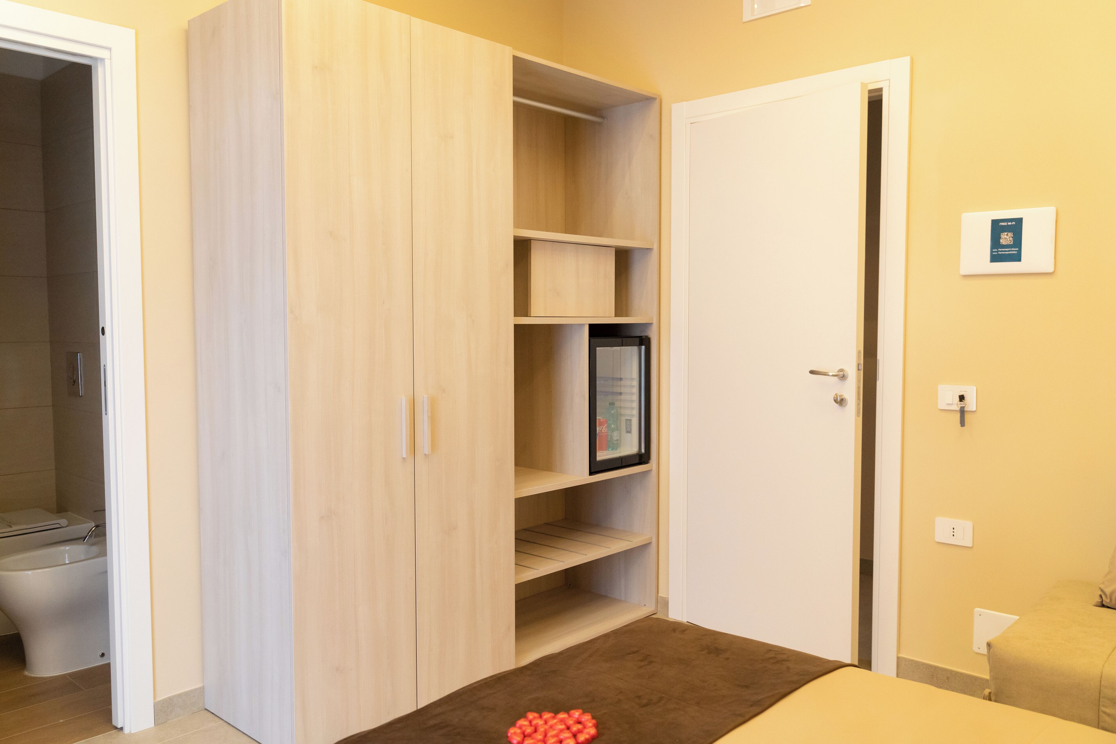 Ein Zimmer mit Holzschrank, Bett, Nachttisch und Toilette.