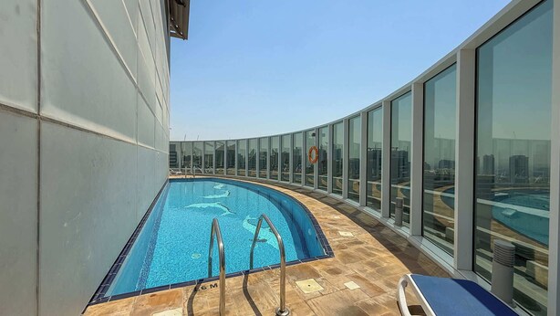 A rooftop pool with clear blue water, surrounded by glass walls offering city views. - StayShort - Stylish Barsha Heights Retreat with Swimming Pool for 2 (Barsha Heights)