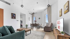 A modern living room with a sofa, coffee table, TV, and a dining area with chairs and a table. - StayShort - Stylish Barsha Heights Retreat with Swimming Pool for 2 (Barsha Heights)
