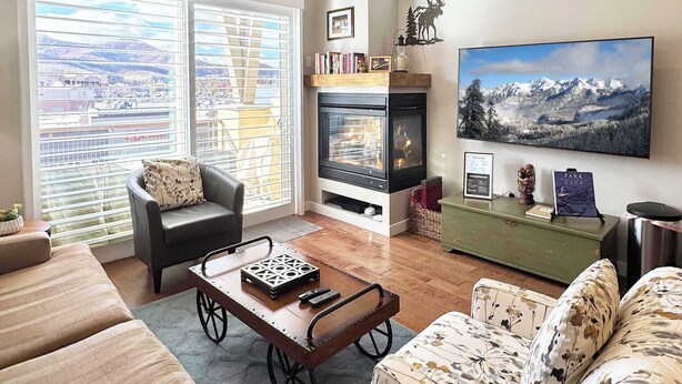 A living room with a fireplace, a large window with a view of mountains, and a sign reading "PARK CITY". - Breathtaking Views, Shopping Center Steps Away! (Park City)