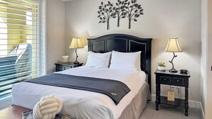 A neatly arranged bedroom with a large bed, two bedside tables, a wall-mounted tree decoration, and a window with blinds. - Breathtaking Views, Shopping Center Steps Away! (Park City)
