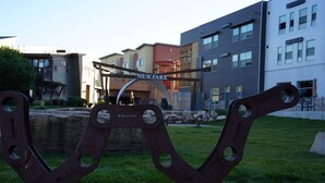 A metal sculpture in a park area with modern buildings in the background. - Breathtaking Views, Shopping Center Steps Away! (Park City)