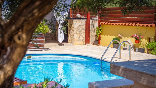 A swimming pool with a stone wall, a wooden fence, and potted plants.